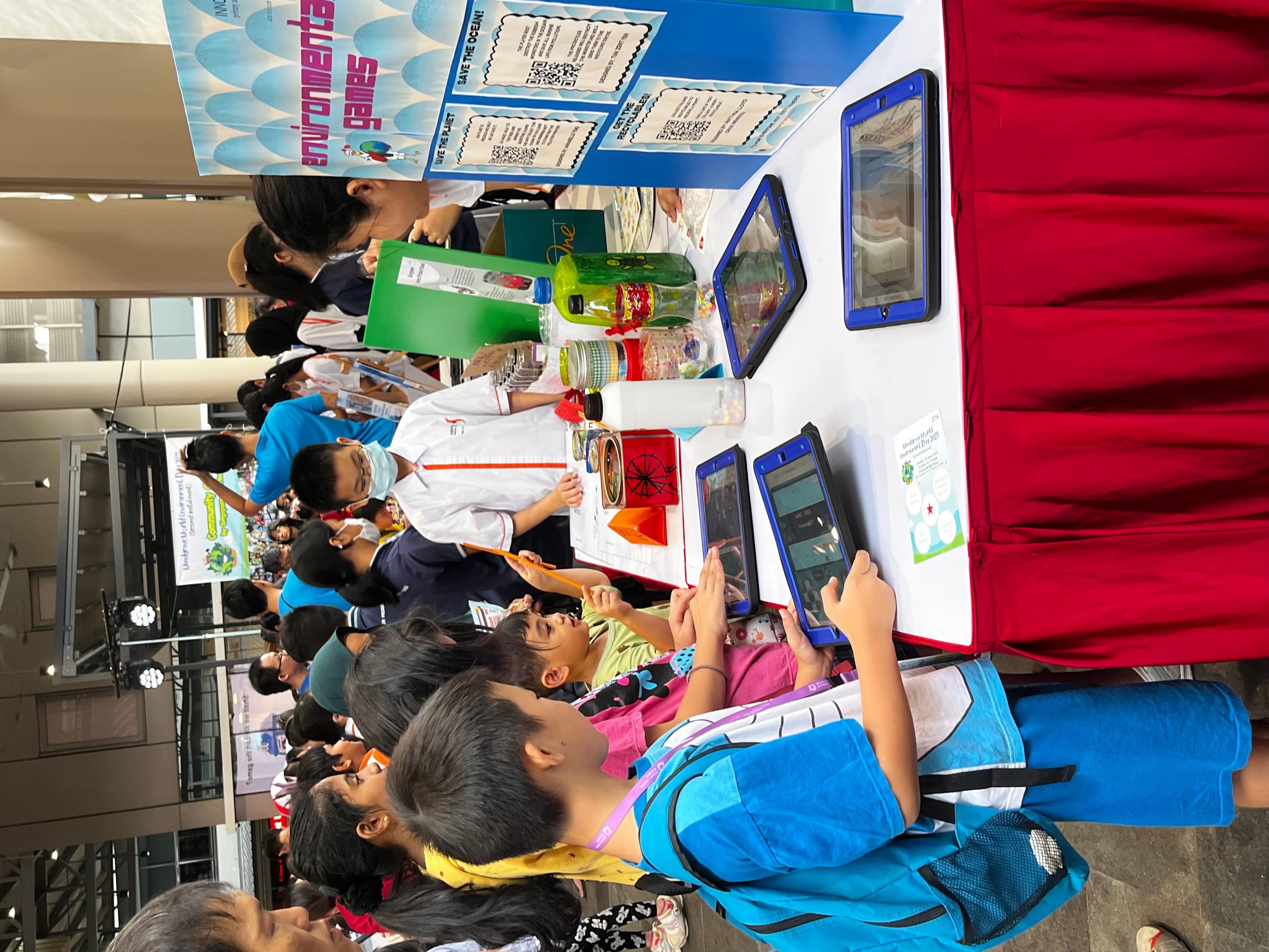 Children interact with tablets at an environmental games booth during a crowded school fair event.